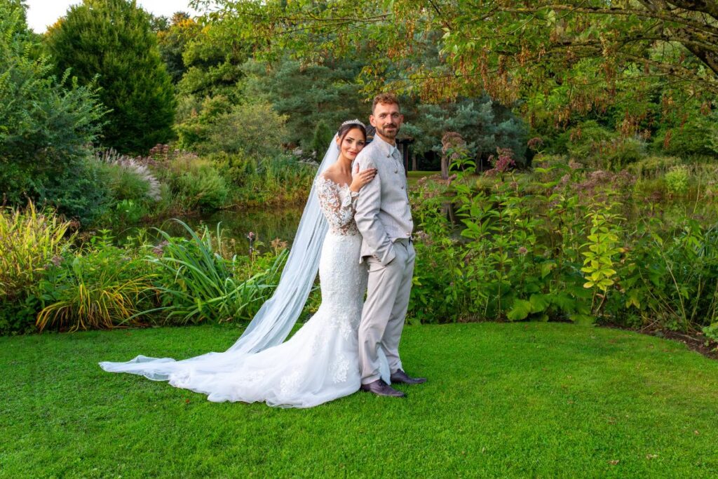 Braut und Bräutigam posieren in eleganter Hochzeitskleidung auf einer grünen Wiese.