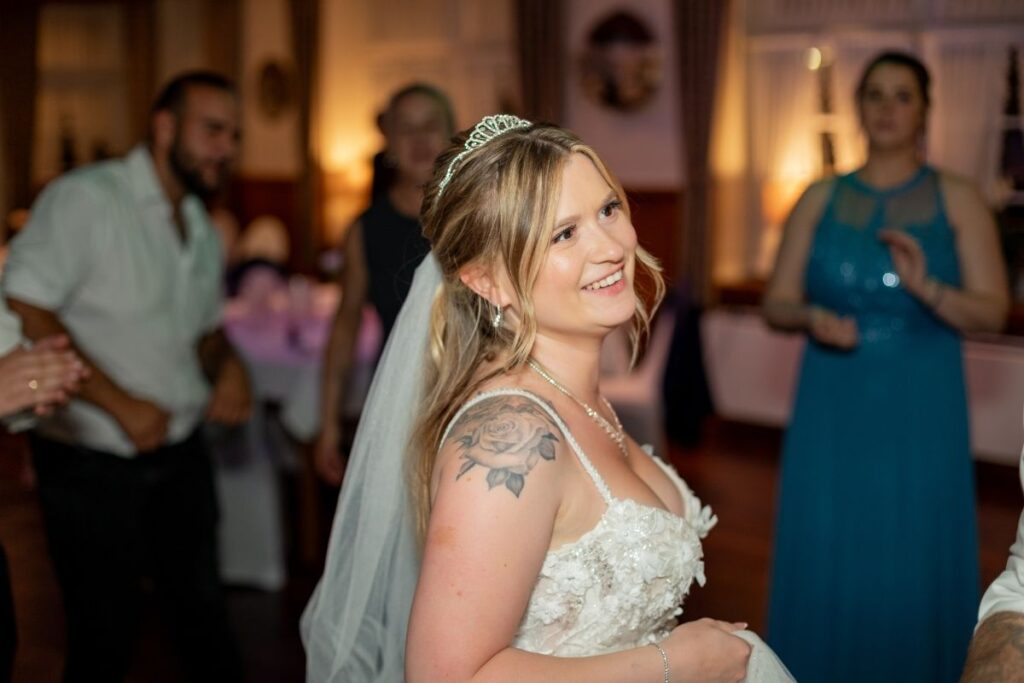 Braut lacht während der Hochzeitsfeier auf der Tanzfläche, umgeben von Gästen