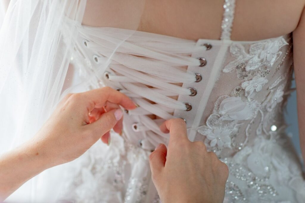 Detailaufnahme vom Schnüren des Brautkleides während der Hochzeitsvorbereitungen