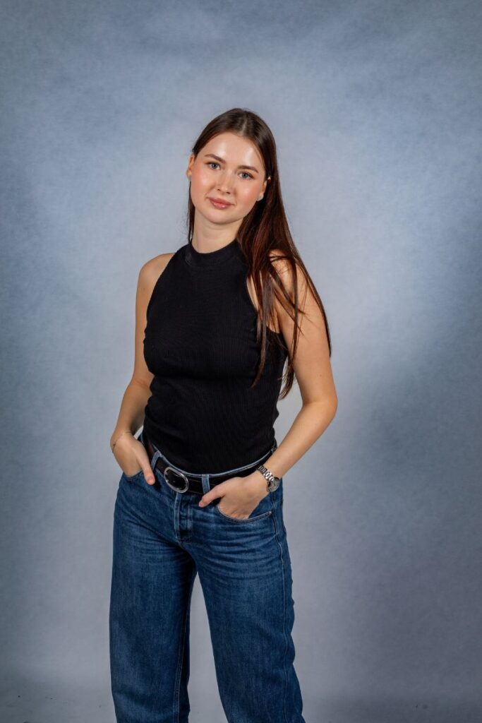 Natürliches Studio-Portrait einer jungen Frau mit langen Haaren, locker stehend vor grauem Hintergrund