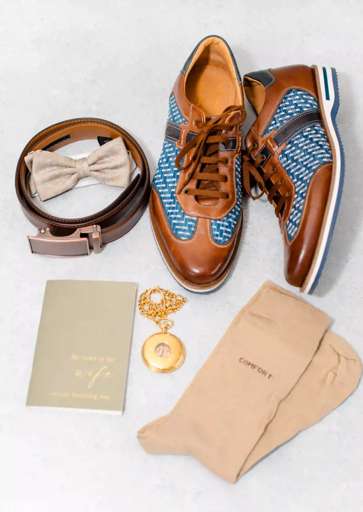 Bräutigam Flatlay mit braunen Lederschuhen, beiger Fliege, Gürtel, goldener Taschenuhr und beigen Socken