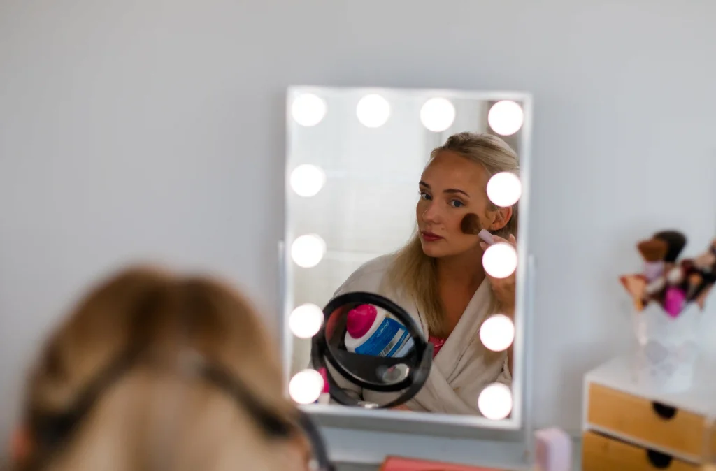 Braut beim Getting Ready trägt Make-up vor einem beleuchteten Schminkspiegel auf