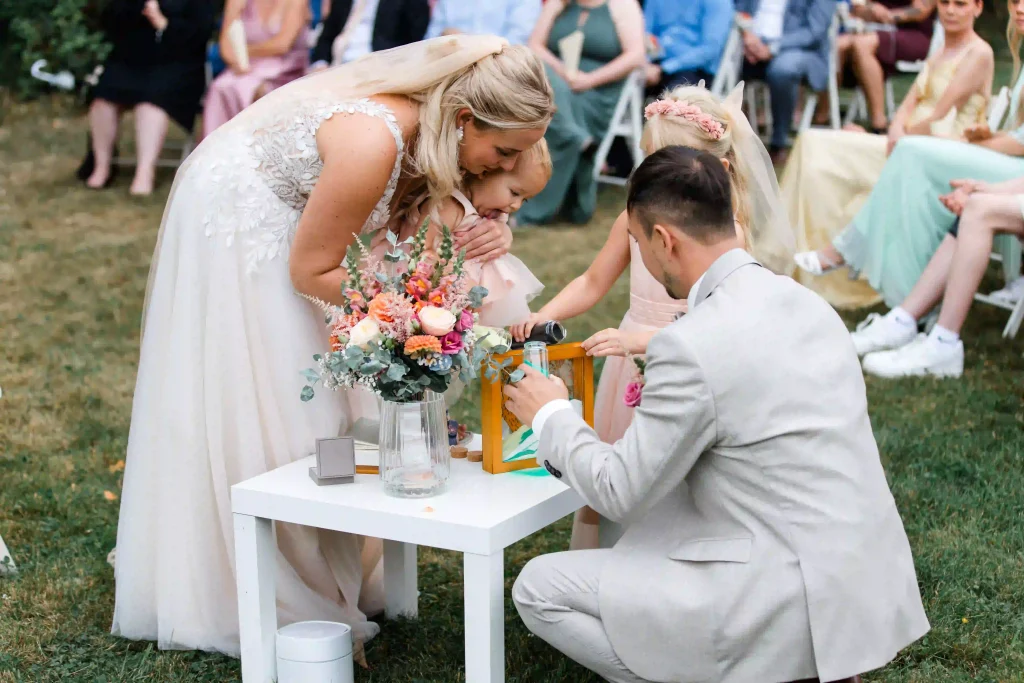 Hochzeit – Brautpaar und Blumenmädchen gestalten gemeinsam ein Erinnerungsritual bei der Trauung im Freien