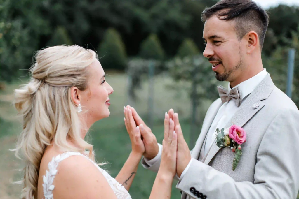 Braut und Bräutigam berühren sich lächelnd mit den Handflächen – natürliches Hochzeitsporträt im Freien