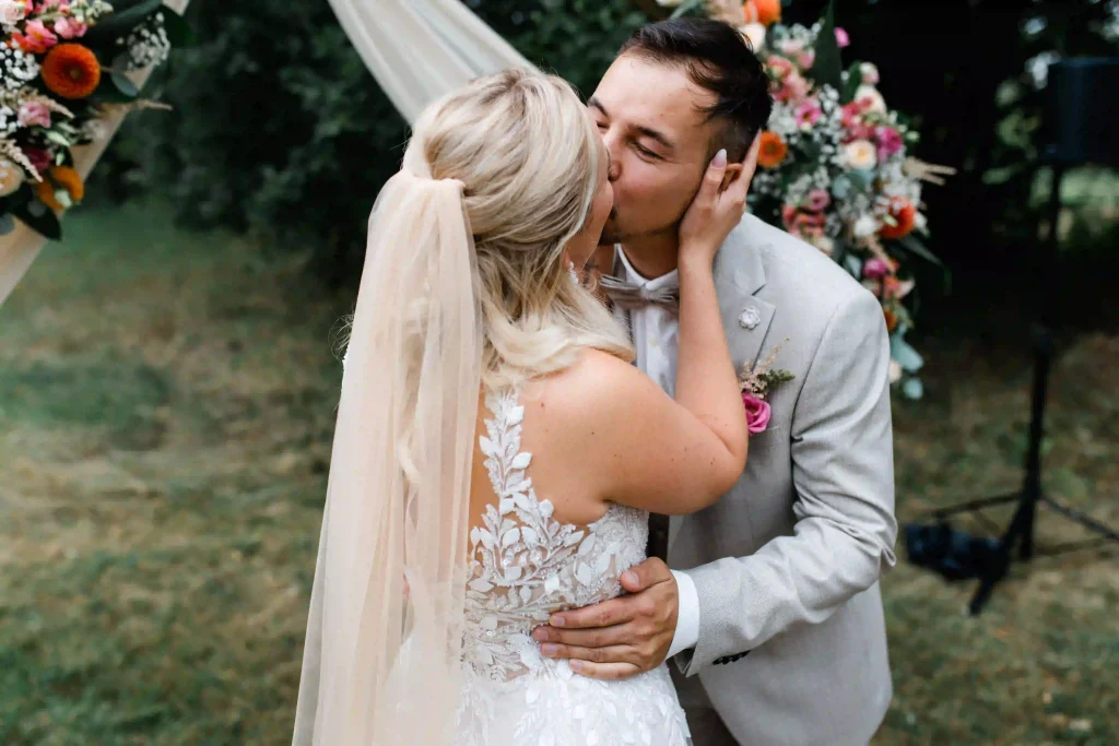 Hochzeit Jaspershof Westerstede – Brautpaar küsst sich romantisch unter einem blumengeschmückten Traubogen