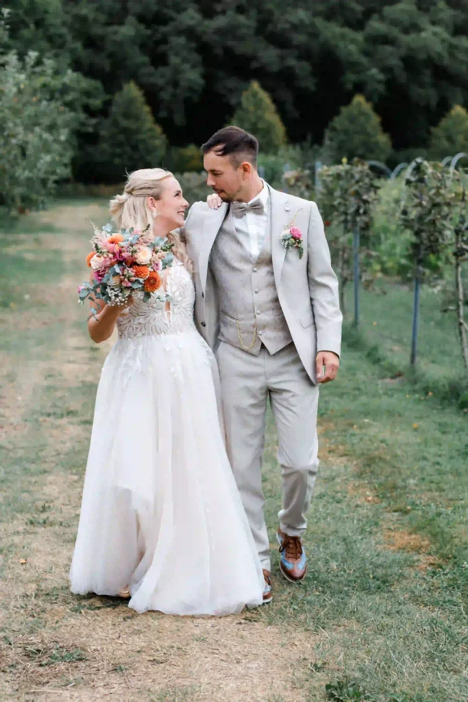 Brautpaar beim Hochzeitsshooting – Braut mit buntem Blumenstrauß und Bräutigam im hellgrauen Anzug
